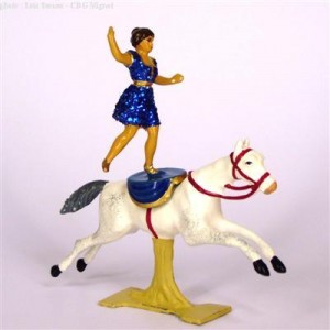 Tin figurine of lady standing, balanced on white circus horse with one leg